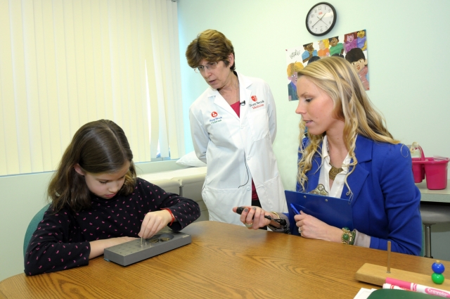 Dr. Lauren Krupp, center, and research coordinator Dana Serafin of the Lourie Center for Pediatric Multiple Sclerosis, administer the grooved peg board test, a measure of fine motor speed and coordination, part of a battery to test the cognitive abilities of patients.